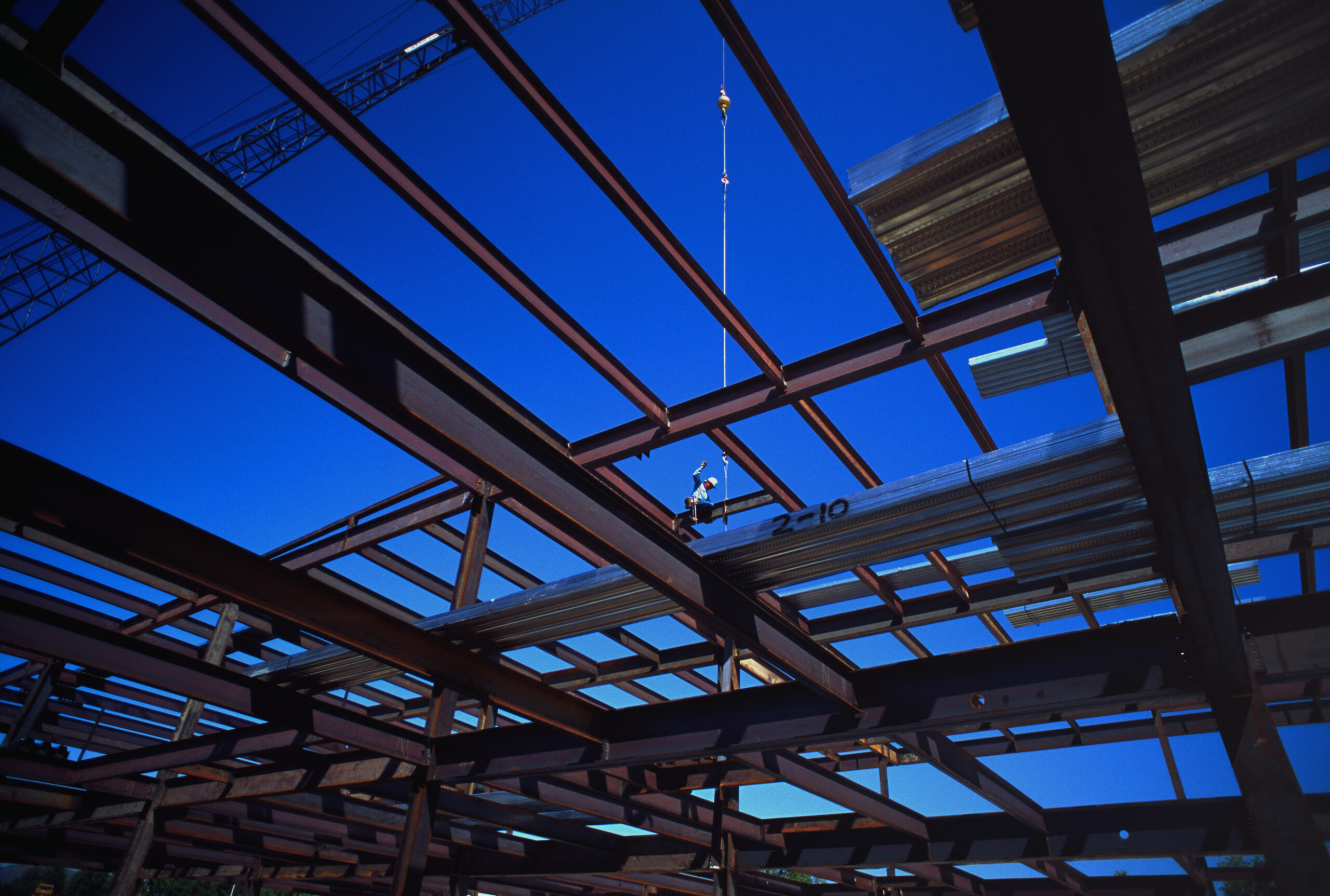 Steel beams that will eventually form the ceiling of a building criss-cross across a clear blue sky.