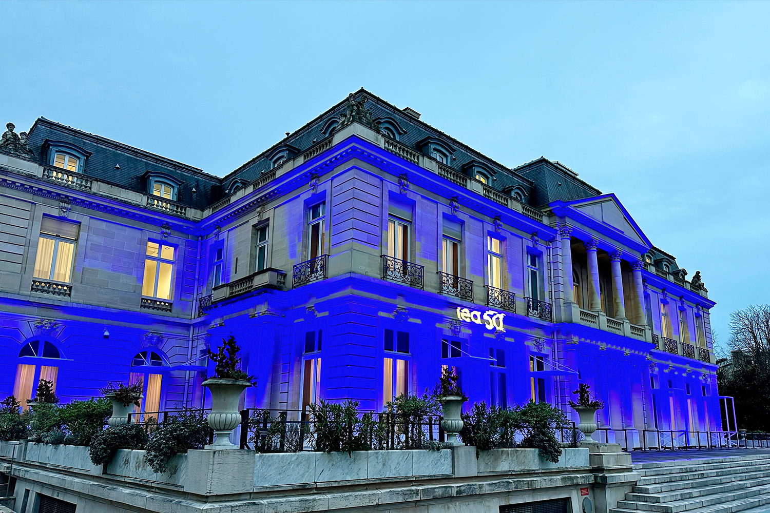 The exterior of a fancy marble building in Paris, lit up with blue lights and the letters 