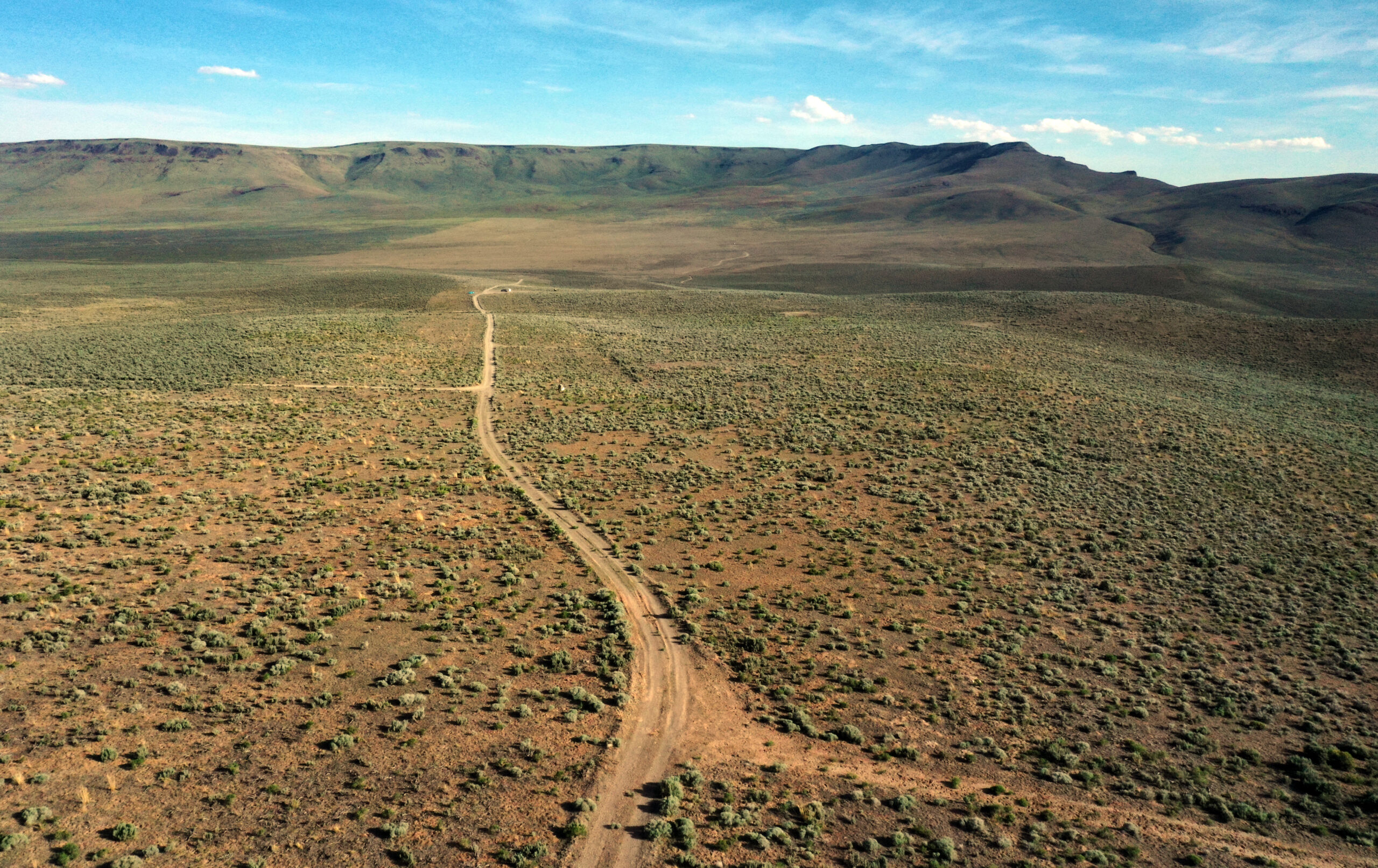 An aerial photo of an arid plain surrounded by mountains with a blue sky above dotted with a few white clouds.