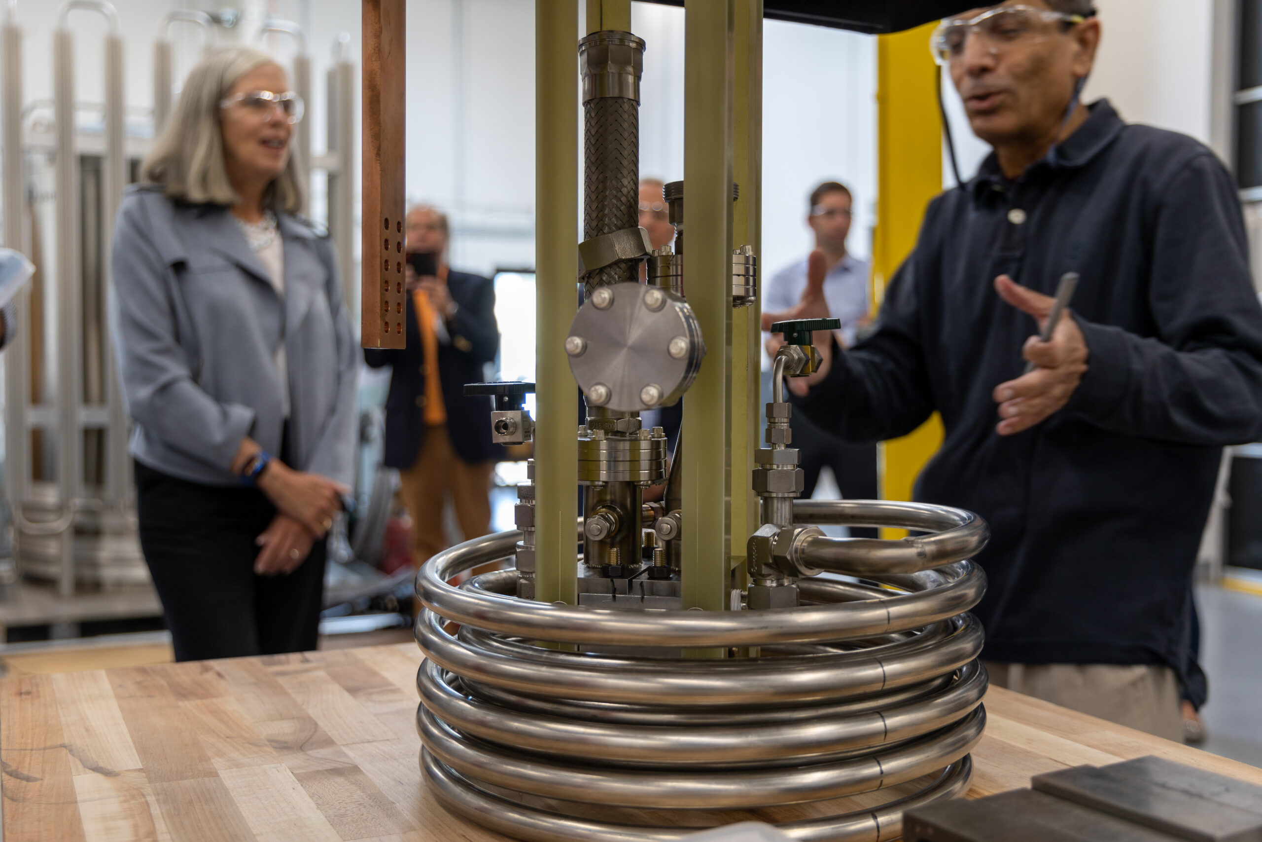 A scientist gestures to a thick coil of metal wires. 