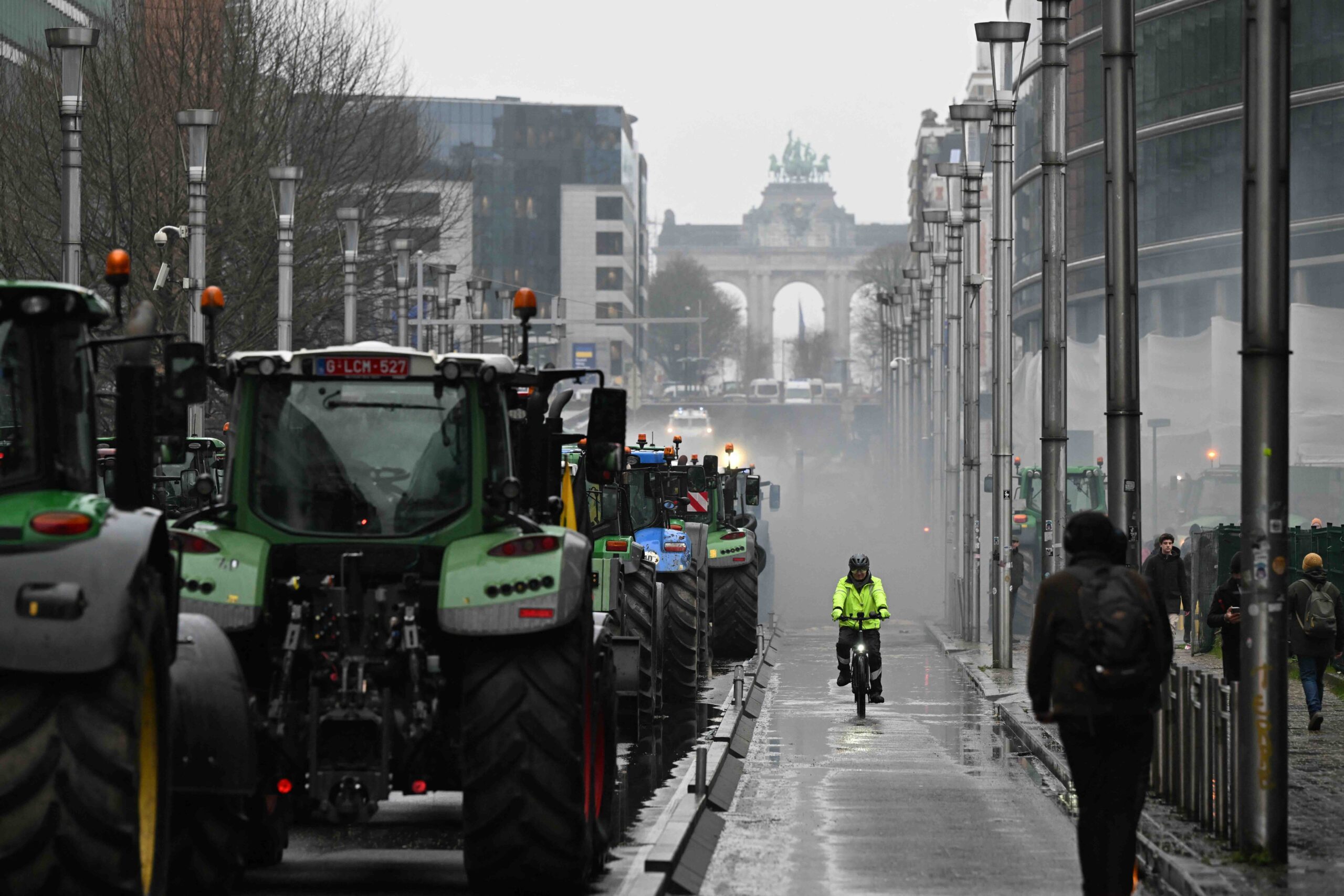 A man rides a bicycle next to tractors that line the streets of Brussels. 