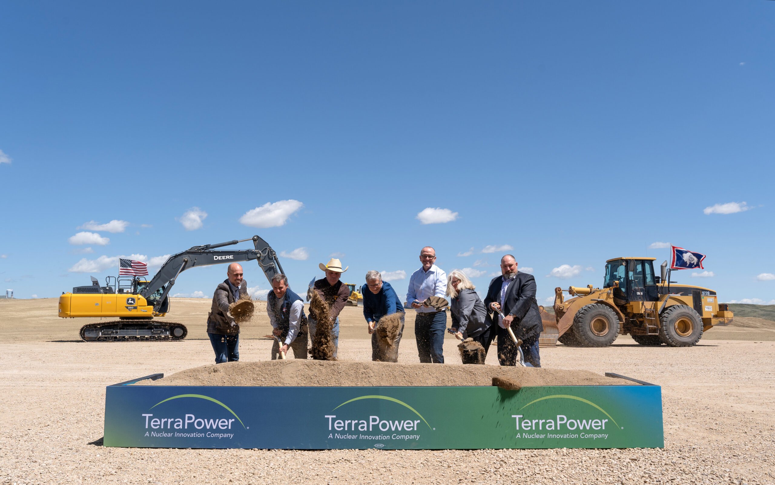 Photo of seven people with shovels throwing some dirt in the air with those shovels in a ceremonial way. Heavy construction equipment is in the background, and there's a banner that says "TerraPower: A Nuclear Innovation Company."